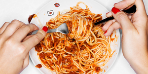 a person with red nails eating a bowl of spaghetti with meat sauce