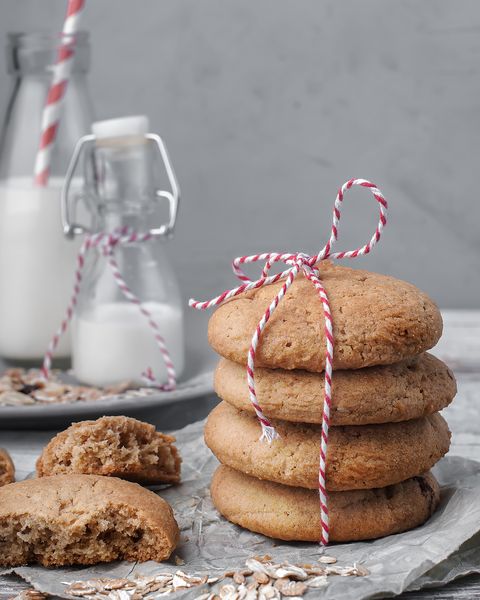 food photography of stack of homemade oatmeal cookies front view close up with a red gift ribbon with bottles of milk on a gray texture concrete background