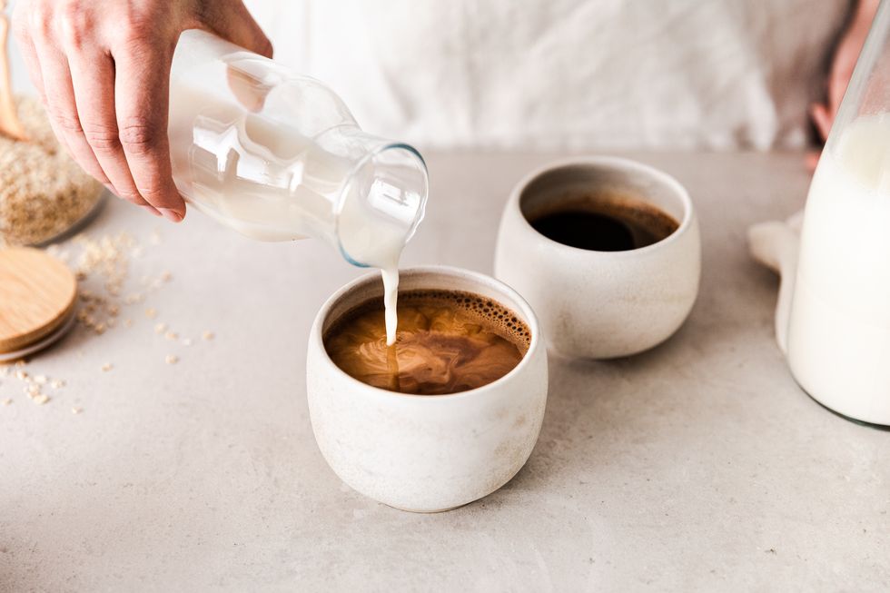 close up of pouring oat milk into black coffee cup making coffee at home