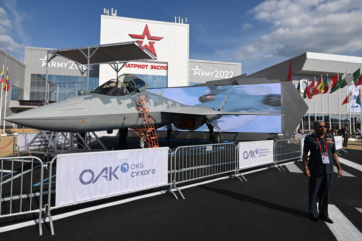 a foreign military official stands in front of a russian jet on display at the army 2022 expo