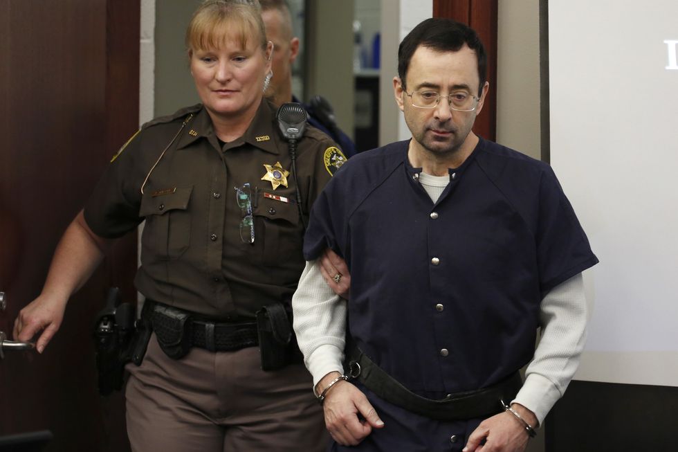 larry nassar held by a security guard as he walks into a courthouse with handcuffs on