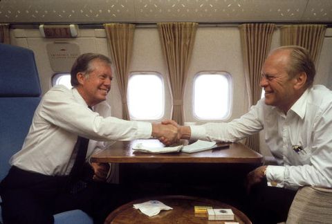 jimmy carter and gerald ford shake hands at a desk on air force one