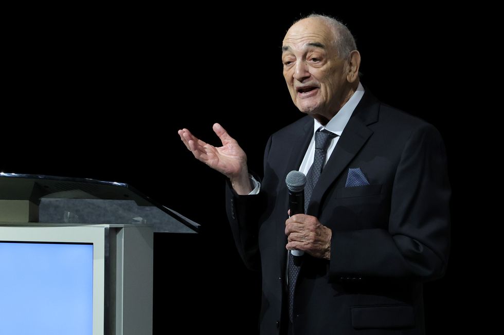 sonny vaccaro wearing a black suit and speaking into a microphone at a podium