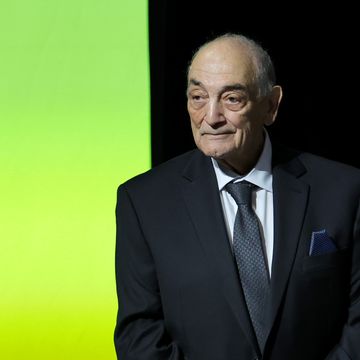 sonny vaccaro wearing a black suit and tie, standing in front of a black and green wall