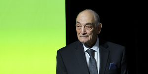 sonny vaccaro wearing a black suit and tie, standing in front of a black and green wall