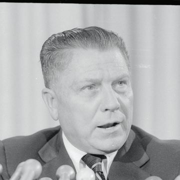 close up portrait of a man who is speaking into several microphones and looking to the right