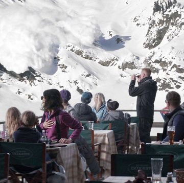 a person speaking to a group of people sitting at tables in front of a mountain