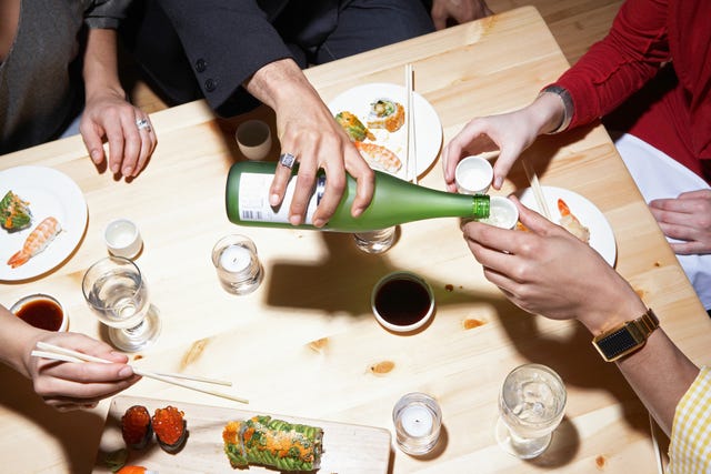four adults eating sushi and drinking sake, mid section, elevated view