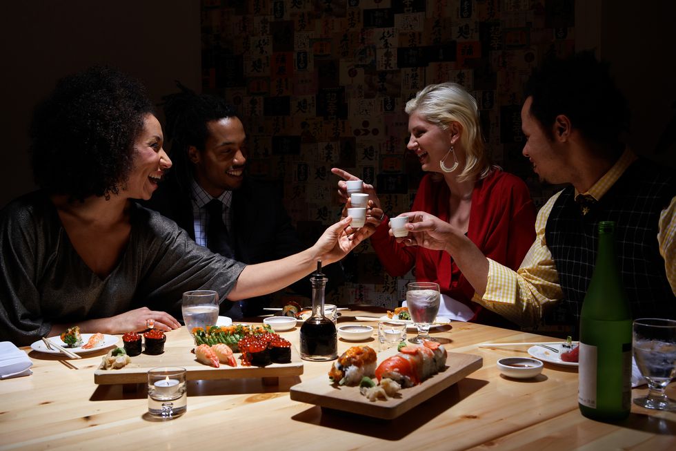 Four adults toasting with sake in sushi bar, laughing