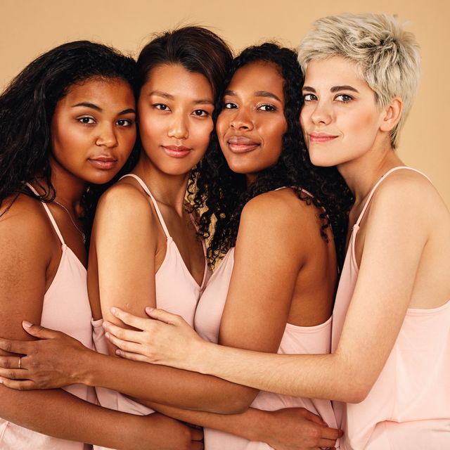 four beautiful women hugging each other in a studio　diverse females standing at background