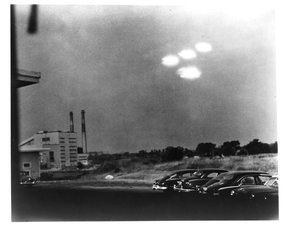 four glowing objects in the sky over a parking lot in a black and white image