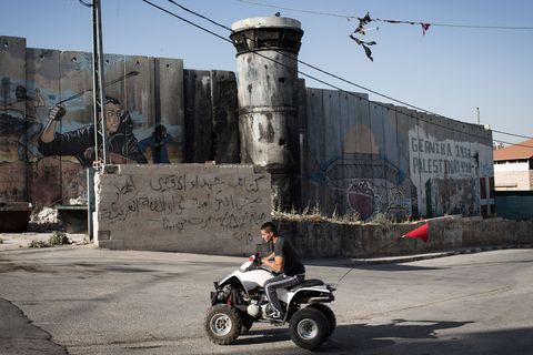 Een jongere rijdt op een vierwieler langs een Isralische wachttoren van waaruit Palestijnse activiteiten in Bethlehem in de gaten worden gehouden