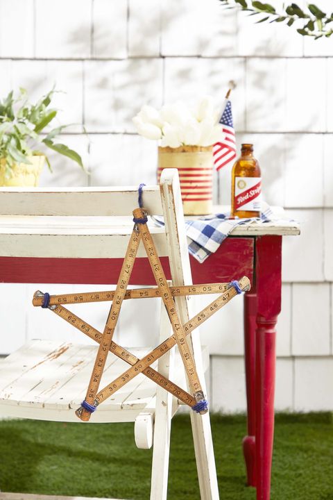 star shape made from a hinged carpenters ruler hung off the back of a rustic white wood folding chair for the 4th of july