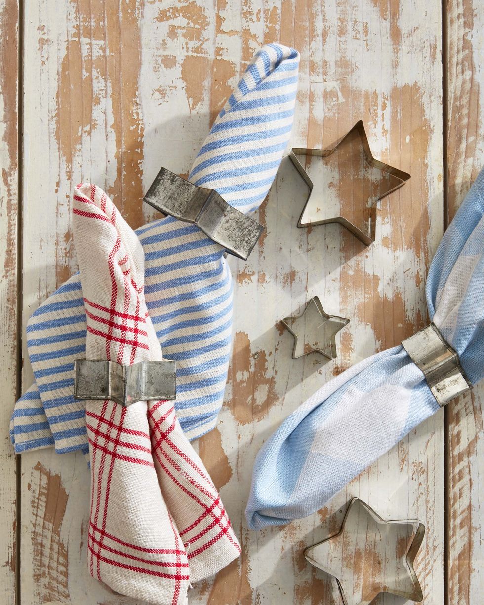 vintage star cookie cutters used as napkin rings threaded with red, white, and blue napkins on a rusting wood table