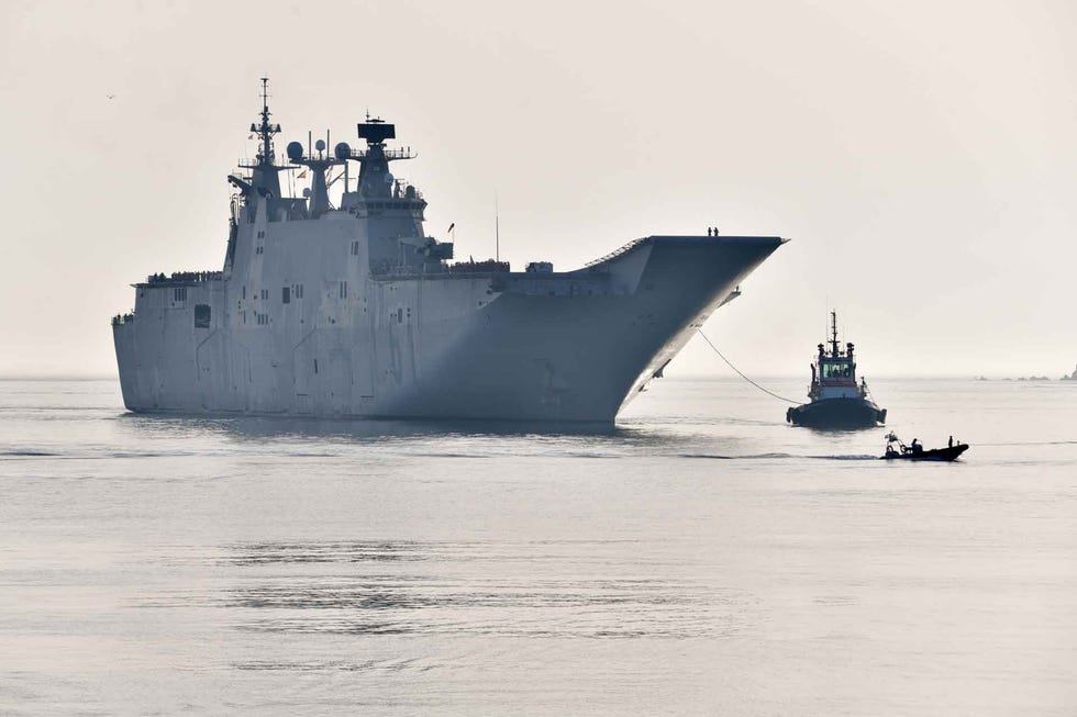military ship being assisted by a tugboat