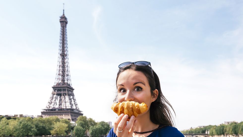 france, paris, staring woman with croissant in front of seine river and eiffel tower