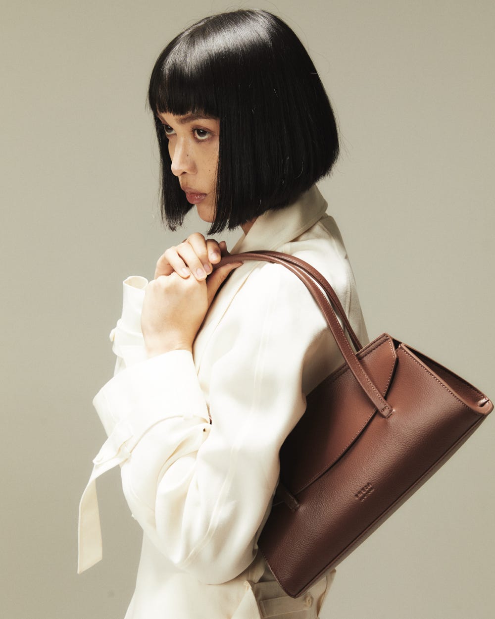 a person holding a brown handbag against a neutral background