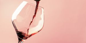 french dry red wine, pours into glass, trendy pink background, space for text, selective focus