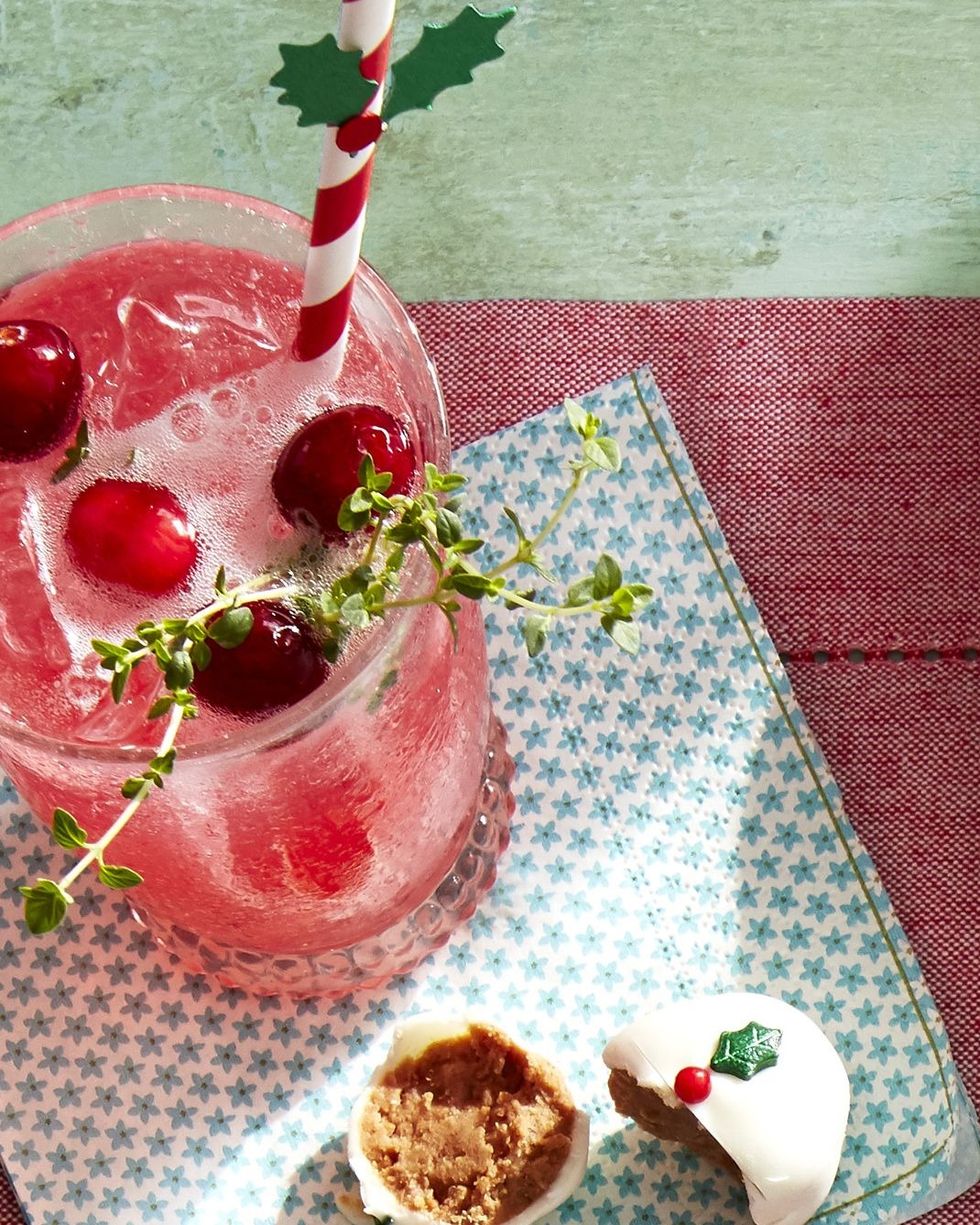 cranberry gin fizz in a glass with ice and fresh cranberries and fresh thyme for garnish