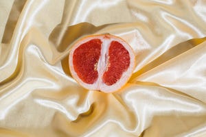 fresh grapefruit on beige soft silk fabric background sex concept women's health, sexuality, erotic tension female vagina and clitoris symbol