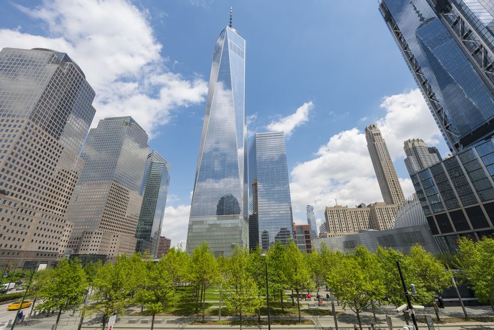 Fresh green trees grow and surround the 9/11 Memorial in spring at Lower Manhattan New York. One World Trade Center and the other lower Manhattan skyscrapers stand behind the 9/11 Memorial. Clouds move over the skyscrapers.