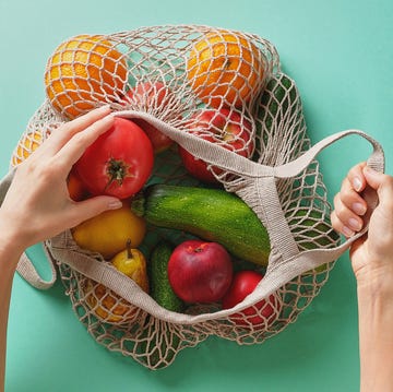 Fresh juicy fruits and vegetables, products in a reusable shopping bag. A girl or woman takes or lays out products from a string bag made from recycled materials on a Green Pastel background. Vegetarianism, Veganism. No plastic. fresh juicy fruits and vegetables, products in a reusable shopping bag a girl or woman takes or lays out products from a string bag made from recycled materials on a green pastel background vegetarianism, veganism no plastic