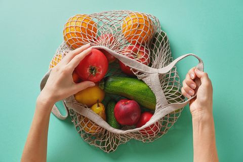 meal prep fresh juicy fruits and vegetables, products in a reusable shopping bag a girl or woman takes or lays out products from a string bag made from recycled materials on a green pastel background vegetarianism, veganism no plastic