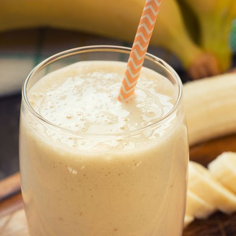 fresh made glass of banana smoothie with straw on wood