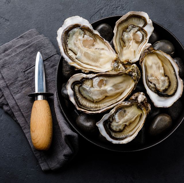 fresh oysters with lemon and knife on stones on dark background