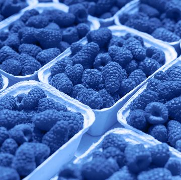 fresh raspberry on a market in paper box containers photographed at an angle from above, image monochrome toned color of the year beautiful blue background for design