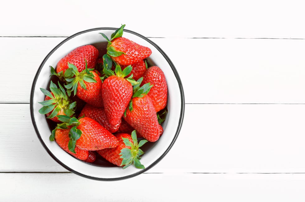 fresh ripe strawberries in a white bowl on a white wooden table