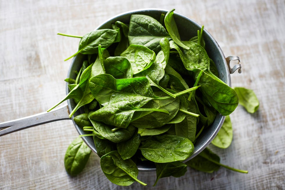 fresh spinach leaves in colander on wood