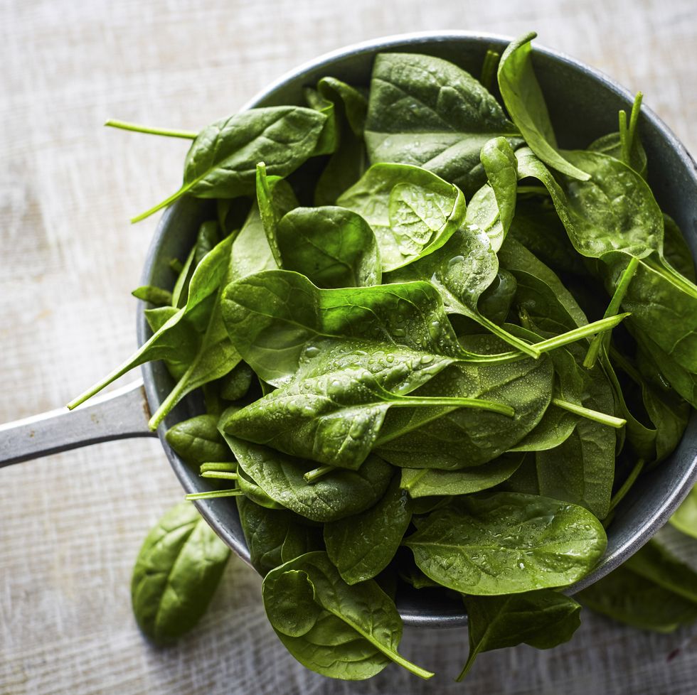 fresh spinach leaves in colander on wood