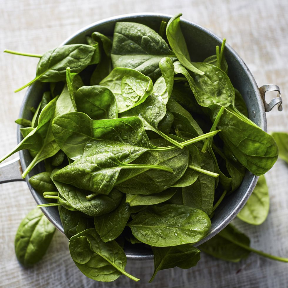Fresh spinach leaves in colander on wood