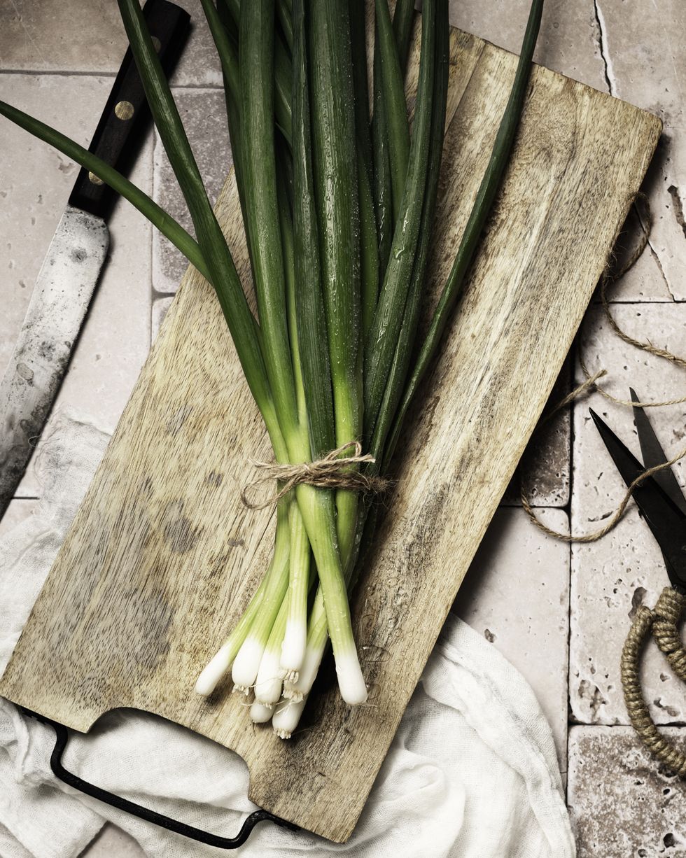 fresh spring onions on rustic wooden board with knife and scissors