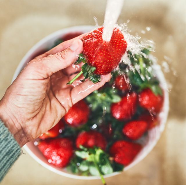fresh strawberries being washed. hand holding ripe berries under running water over a white colander.
