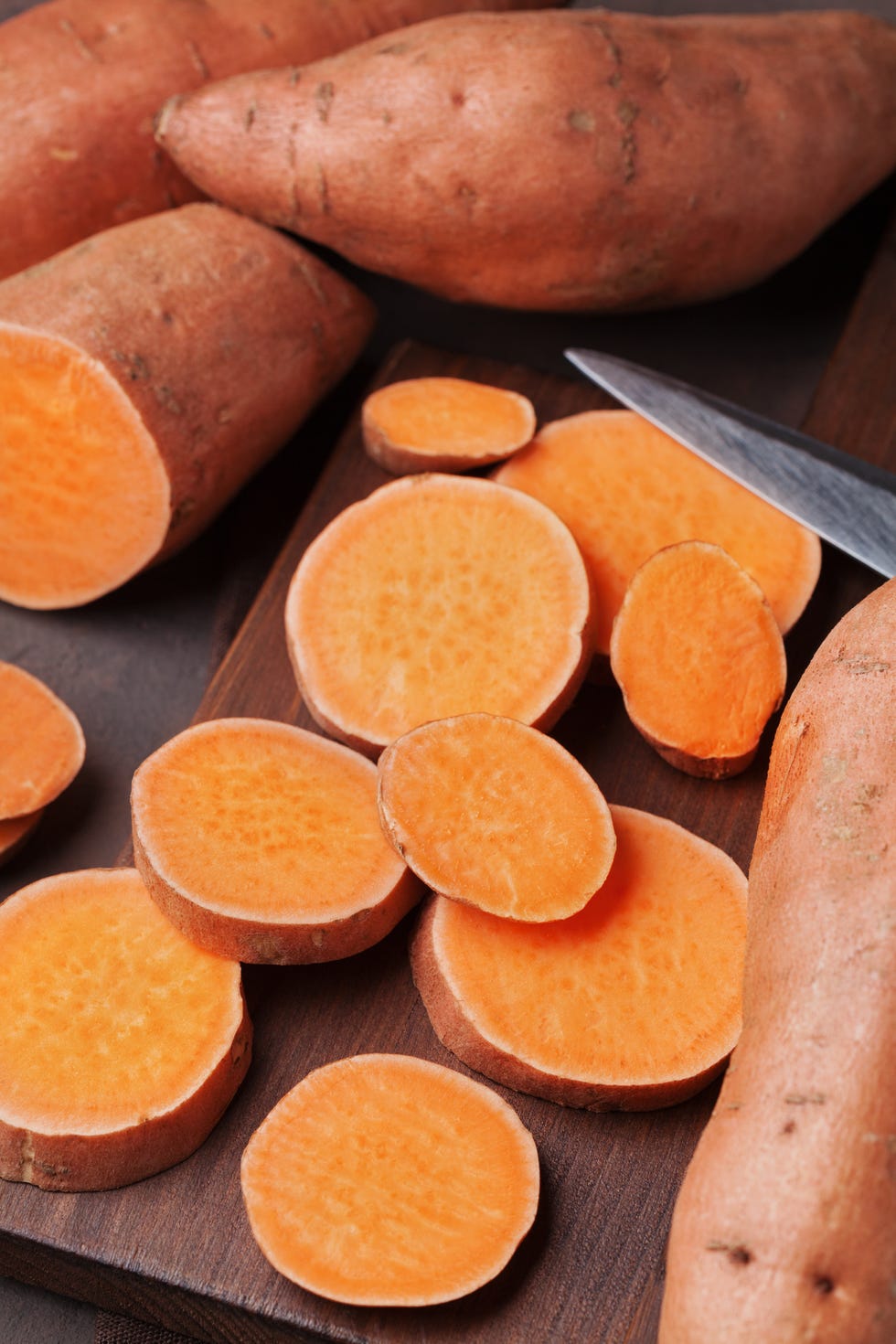 fresh sweet potatoes whole and sliced on wooden kitchen board from above
