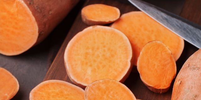 fresh sweet potatoes whole and sliced on wooden kitchen board from above organic food
