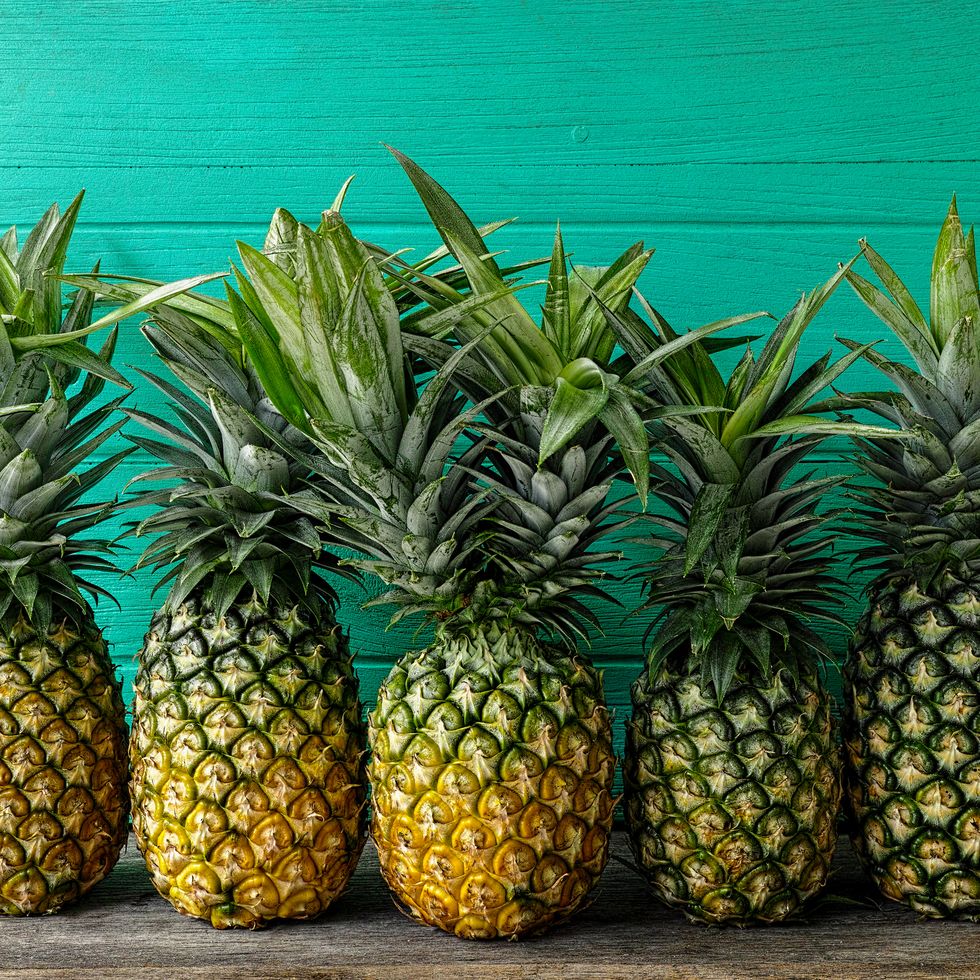Fresh two-headed tropical pineapple standing in the middle of a row of pineapples, on a rustic wooden table against a turquoise wooden walled background.