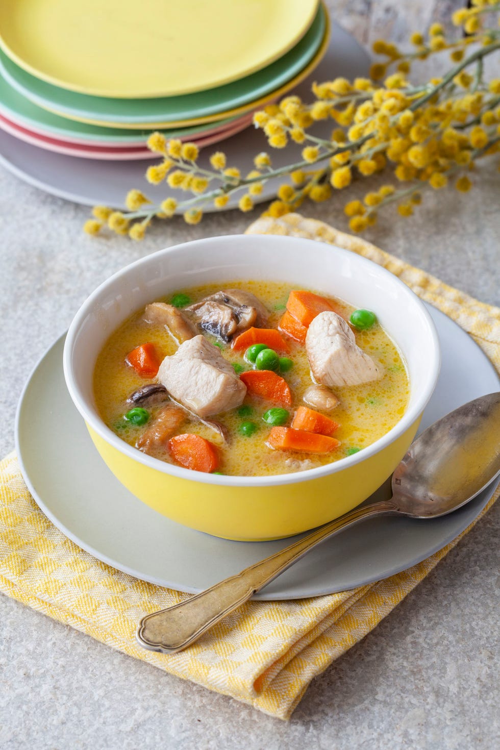 cuenco amarillo con un guiso de pollo y vegetales como zanahoria y guisantes