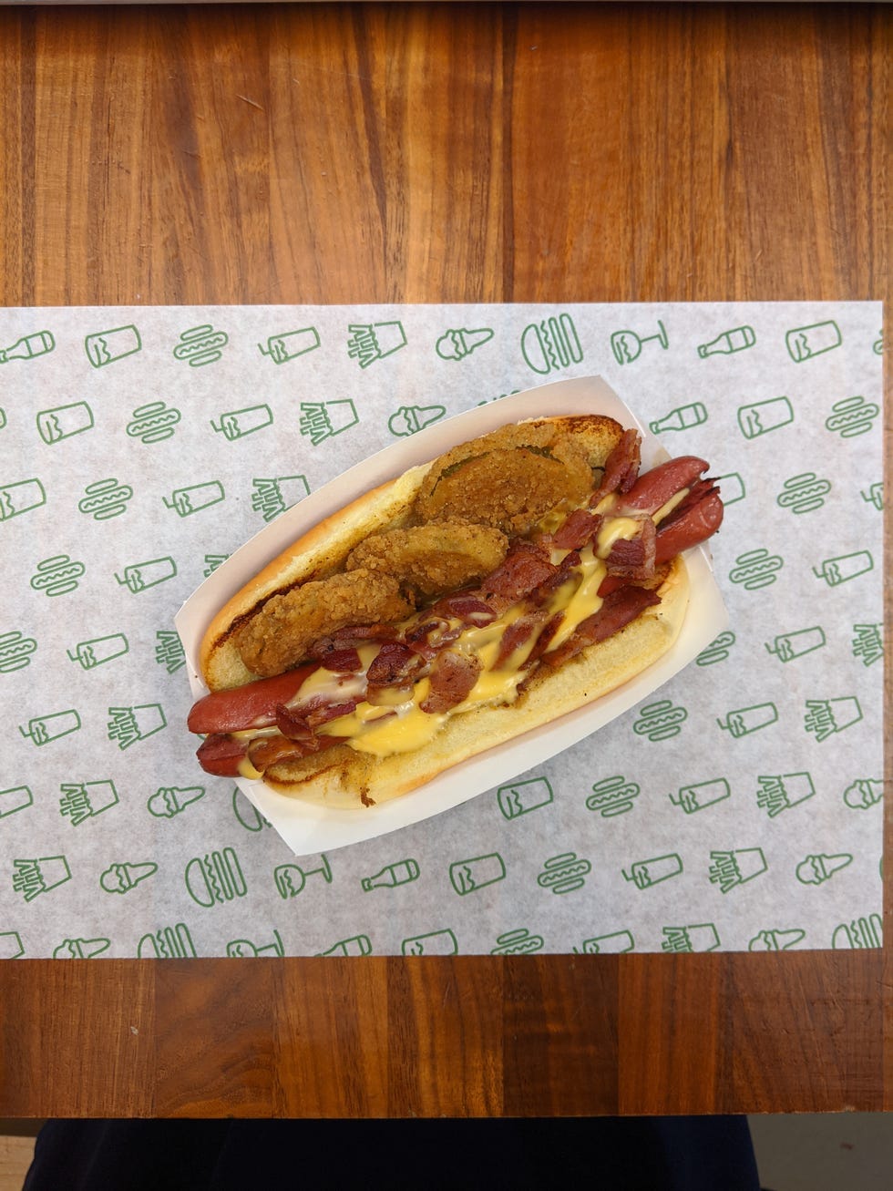 hot dog topped with fried pickles, chopped applewood smoked bacon and melted cheese