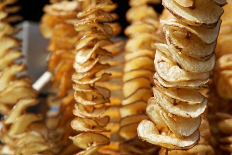 fried potato chips on stick, spiral potatoes fried, on wooden sticks, spiral selling food at the market unhealthy fried street food