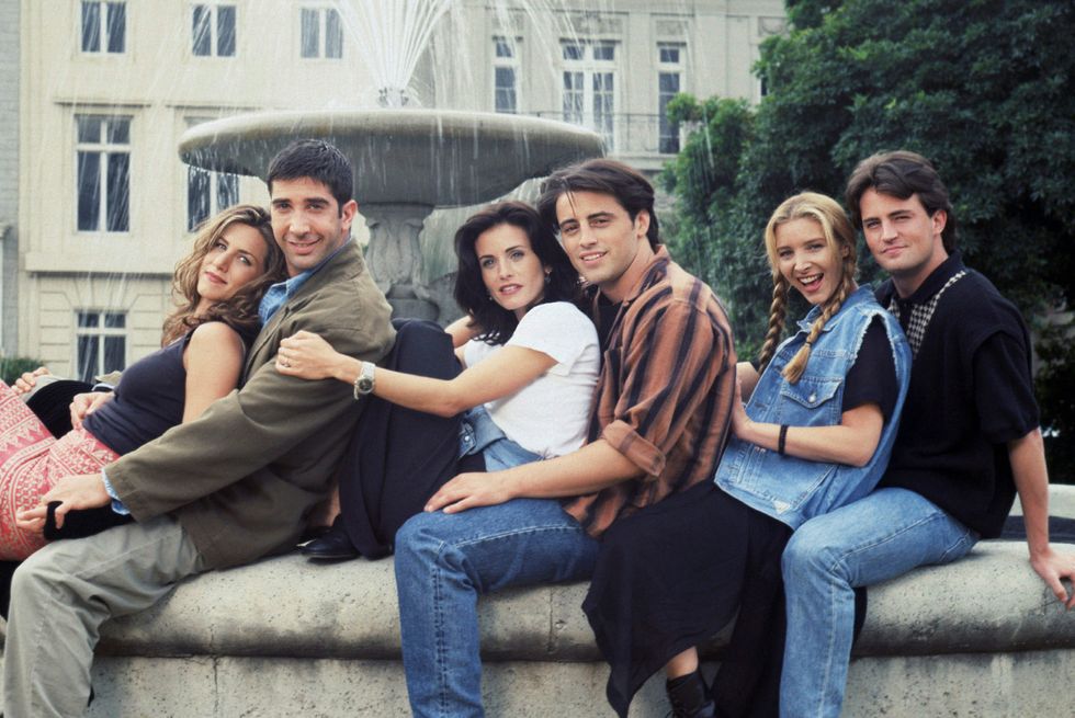 friends cast sitting together next to fountain