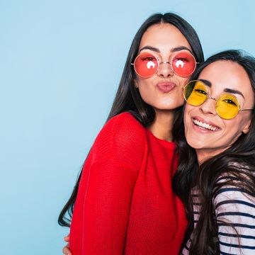 Friends forever. Two cute lovely girl friends in sunglasses posing with smile on blue background
