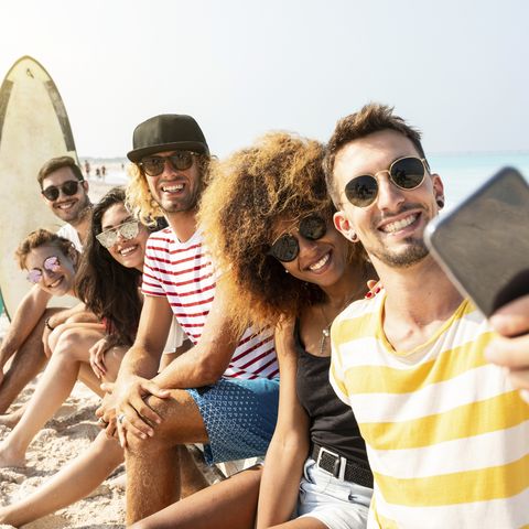 Friends sitting on the beach, having fun, taking selfies