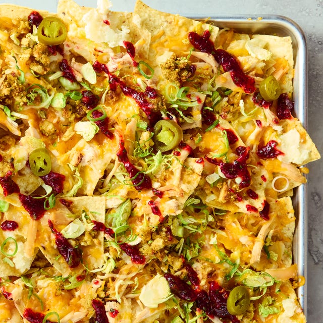 tortilla chips on a sheet tray topped with melted cheese, turkey, stuffing, cranberry sauce, and jalapenos