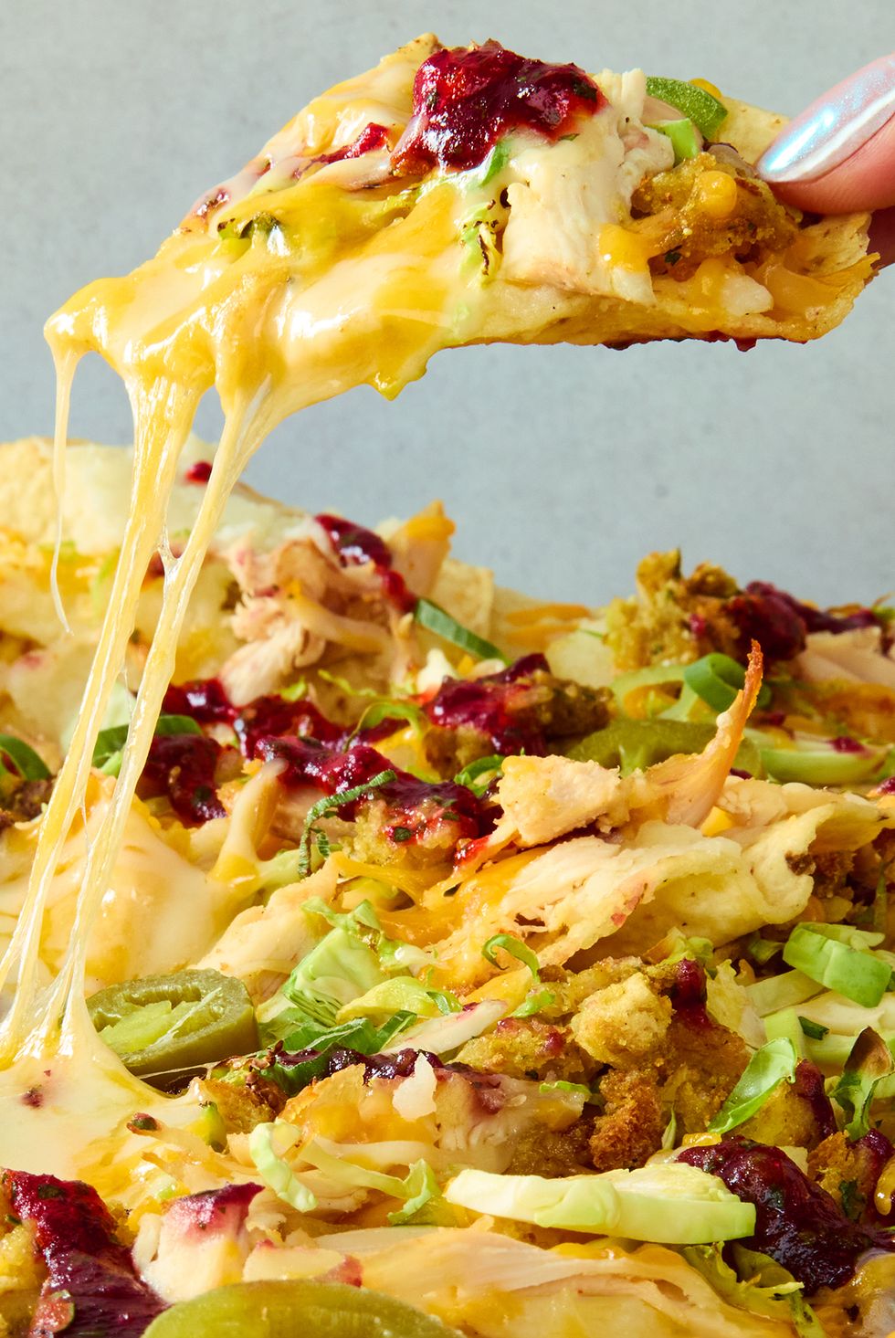 tortilla chips on a sheet tray topped with melted cheese, turkey, stuffing, cranberry sauce, and jalapenos