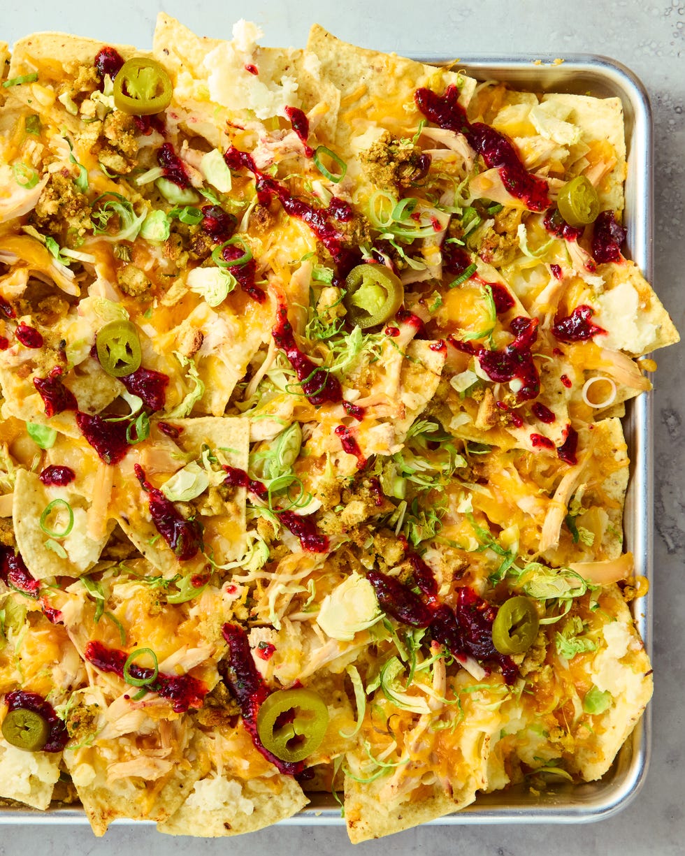 tortilla chips on a sheet tray topped with melted cheese, turkey, stuffing, cranberry sauce, and jalapenos