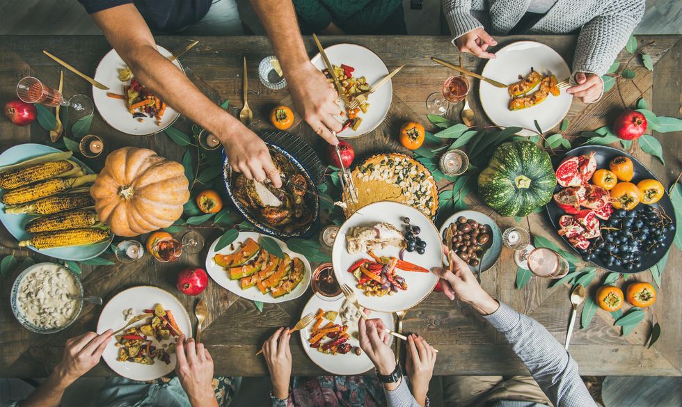 overhead view of thanksgiving day table with turkey, pumpkin pie, roasted seasonal vegetables and fruit and people filling plates and eating