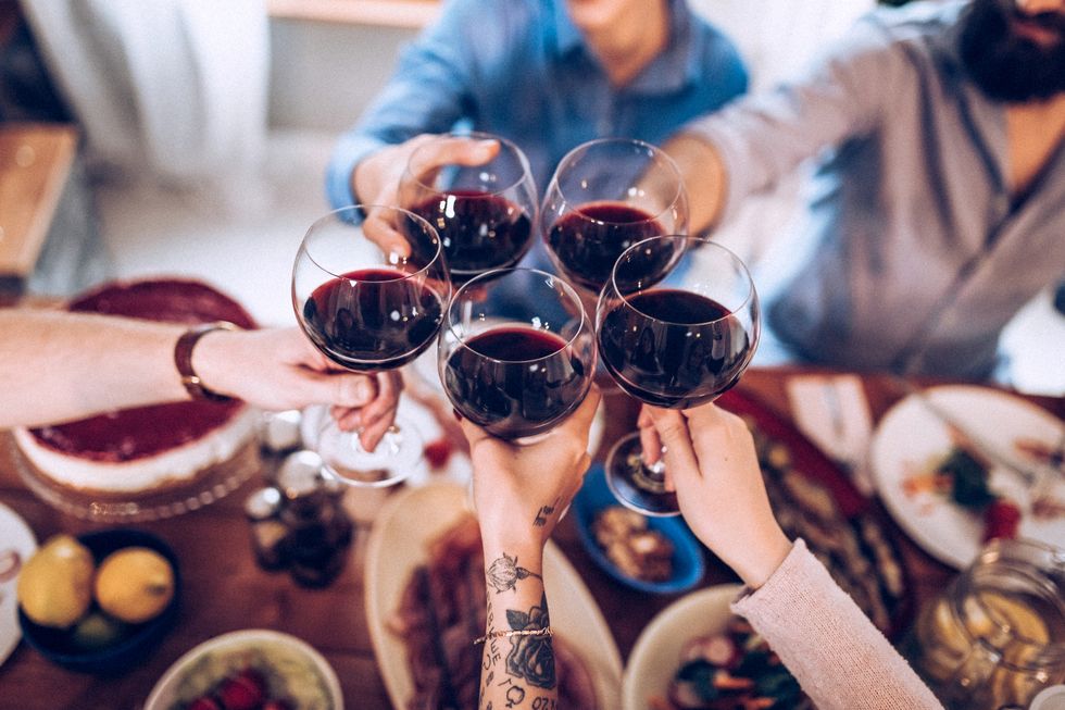 hands and arms of five people toasting with glasses of ed wine over a dinner table